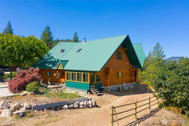 view of front of house with log exterior, metal roof, a standing seam roof, and fence