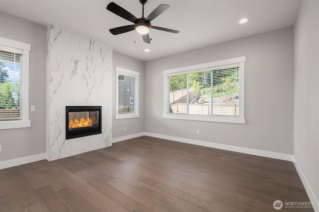 unfurnished living room with recessed lighting, a premium fireplace, baseboards, and wood finished floors