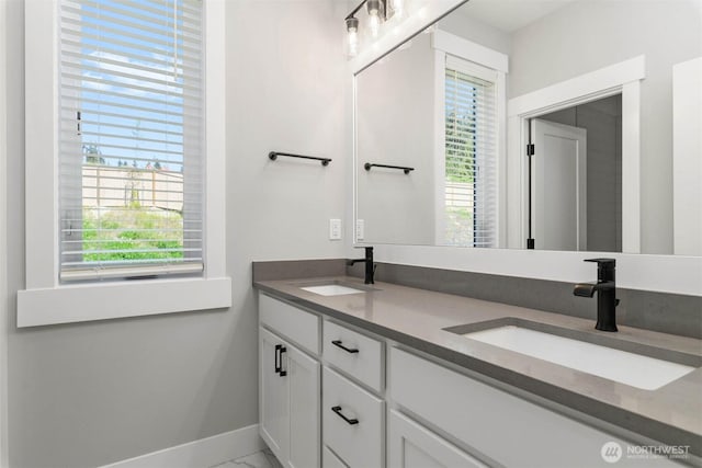 full bath with double vanity, marble finish floor, baseboards, and a sink