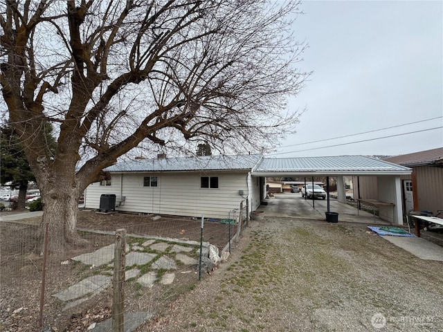 exterior space featuring fence, driveway, central AC, a carport, and metal roof