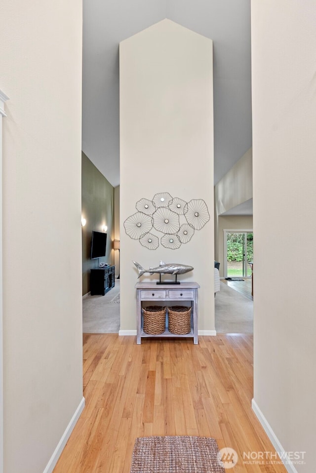 hallway with a high ceiling, wood finished floors, and baseboards