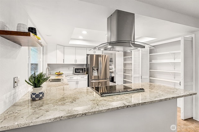 kitchen featuring light stone counters, a peninsula, island range hood, stainless steel appliances, and a sink