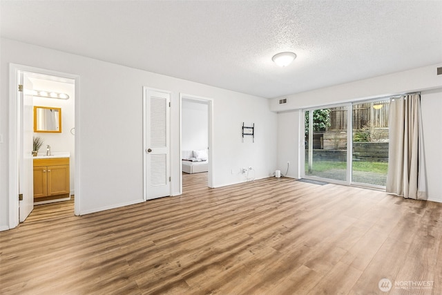 unfurnished bedroom with a sink, light wood-style floors, a textured ceiling, access to outside, and connected bathroom