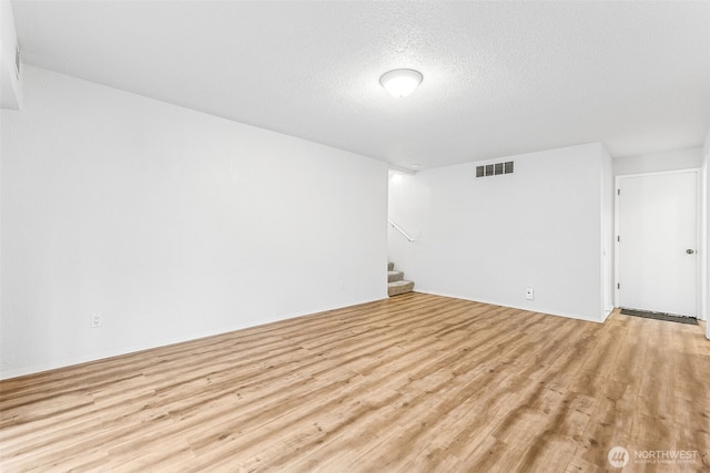 spare room with a textured ceiling, stairway, visible vents, and light wood-type flooring