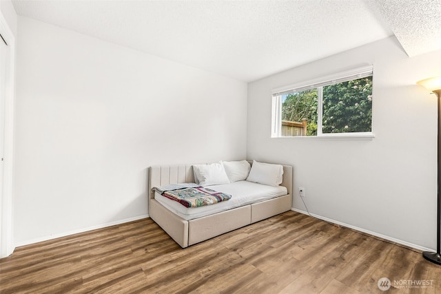 living area with baseboards, a textured ceiling, and wood finished floors