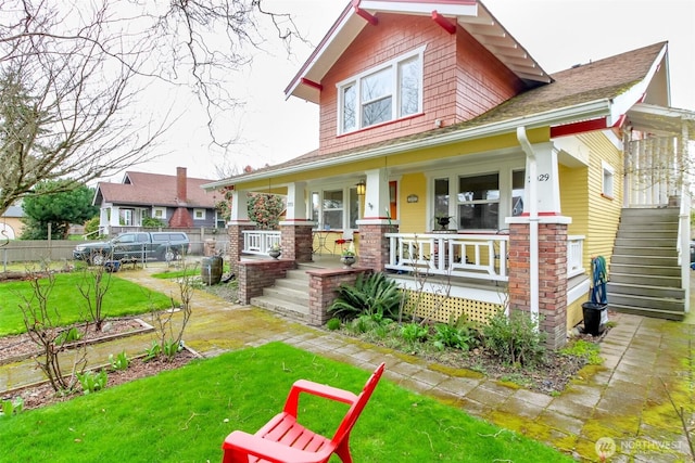 craftsman house with stairs, covered porch, a front yard, and fence