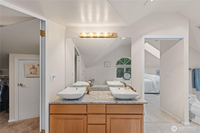 ensuite bathroom featuring a sink, lofted ceiling, and double vanity