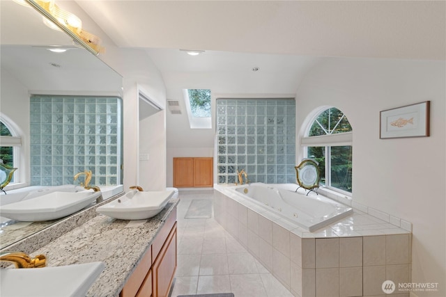 bathroom with tile patterned flooring, vaulted ceiling with skylight, a jetted tub, and a sink