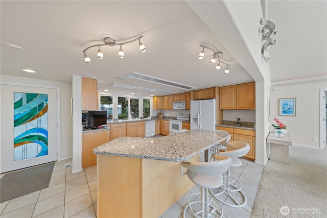 kitchen featuring white appliances, light tile patterned floors, light stone countertops, a kitchen island, and a kitchen bar