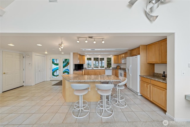 kitchen with light tile patterned floors, white appliances, a breakfast bar, and a center island