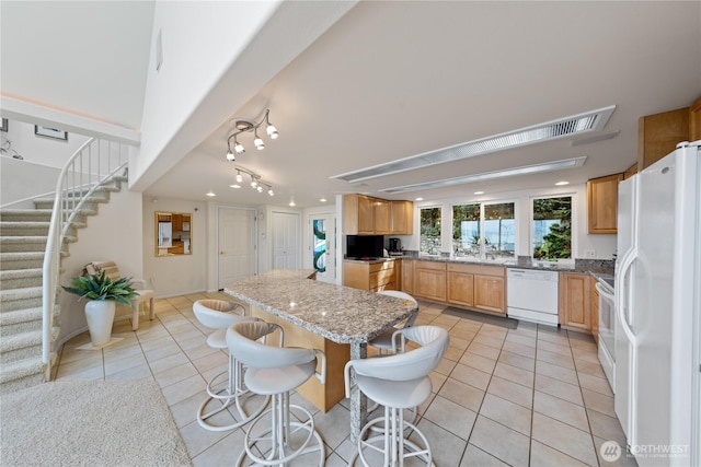 kitchen featuring light tile patterned floors, white appliances, a breakfast bar, and a center island