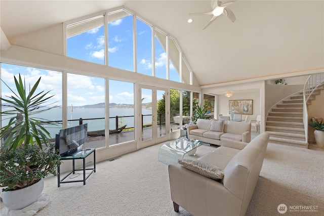 carpeted living room with stairs, ceiling fan, visible vents, and high vaulted ceiling