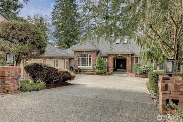 view of front of home featuring an attached garage, brick siding, driveway, and roof with shingles