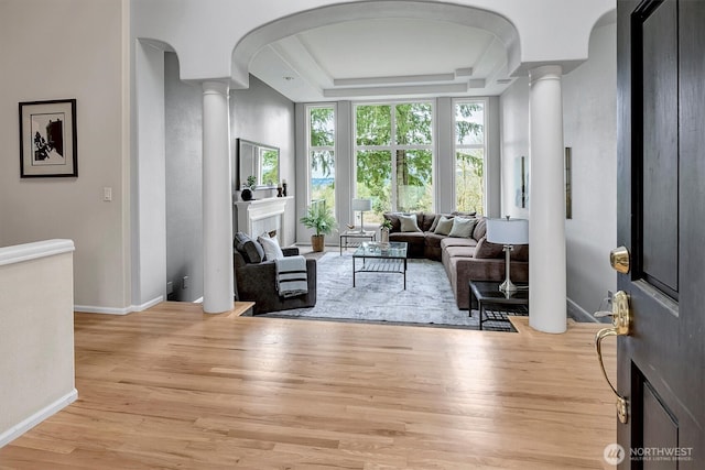 living room with wood finished floors, baseboards, a tray ceiling, decorative columns, and arched walkways