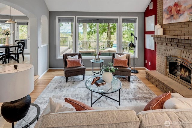 living area featuring vaulted ceiling, plenty of natural light, a fireplace, and light wood-type flooring