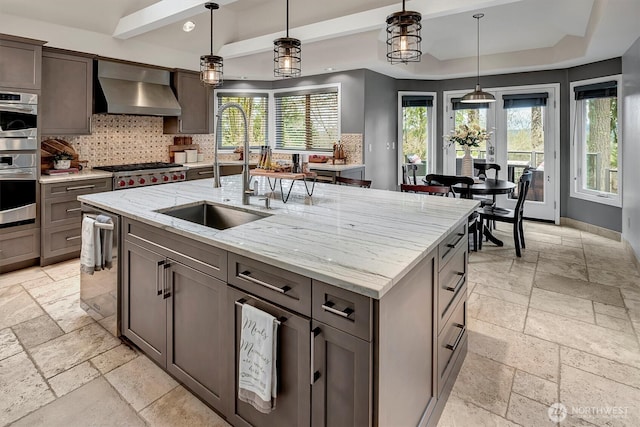 kitchen with a sink, wall chimney exhaust hood, appliances with stainless steel finishes, and stone tile flooring