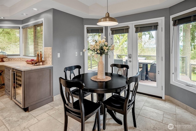 dining room with a raised ceiling, stone tile floors, french doors, wine cooler, and baseboards