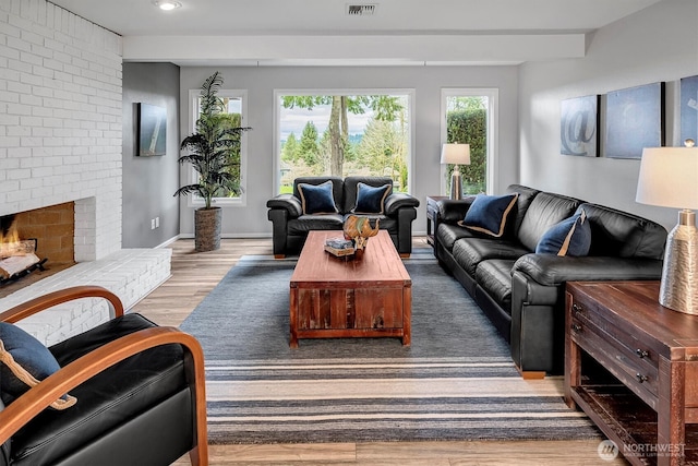 living area with a brick fireplace, wood finished floors, visible vents, and baseboards