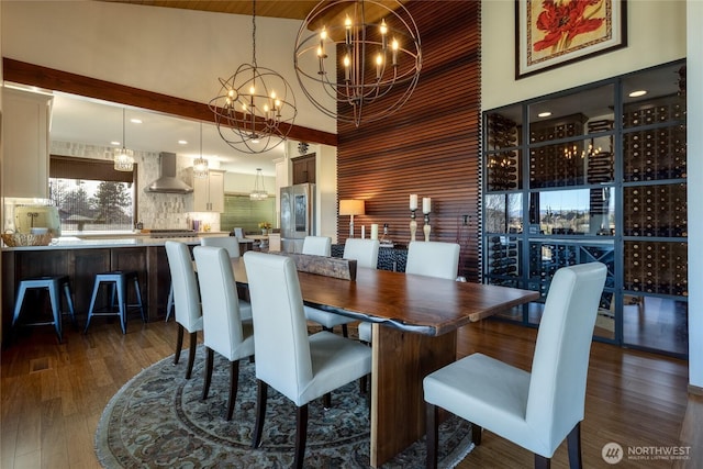 dining area featuring dark wood-style floors, a dry bar, a high ceiling, and an inviting chandelier