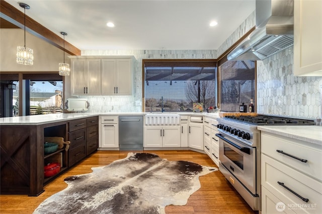 kitchen with stainless steel appliances, wall chimney exhaust hood, light wood-style floors, and a sink