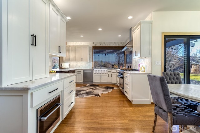 kitchen featuring light wood-style flooring, appliances with stainless steel finishes, wall chimney exhaust hood, light countertops, and decorative backsplash