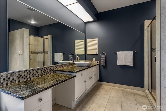 bathroom with tile patterned flooring, backsplash, baseboards, a stall shower, and vanity