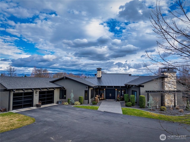 view of front of property with a standing seam roof, a chimney, a garage, aphalt driveway, and metal roof