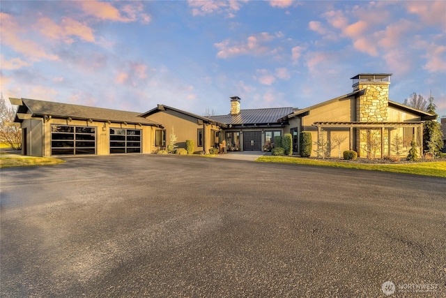 mid-century modern home with metal roof, a garage, driveway, and a chimney