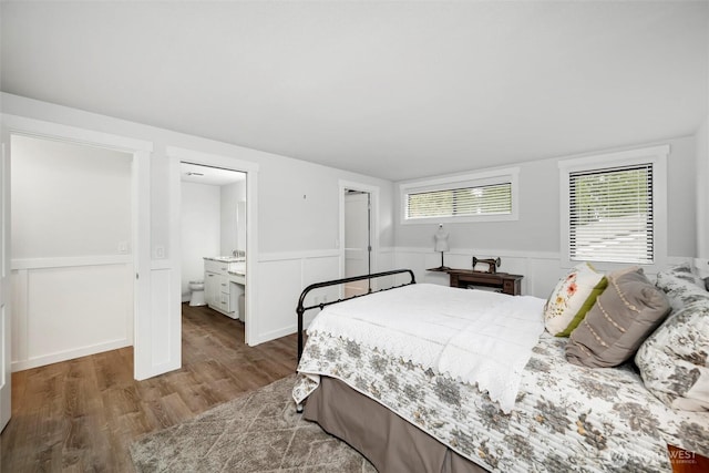 bedroom featuring ensuite bathroom, wood finished floors, and wainscoting