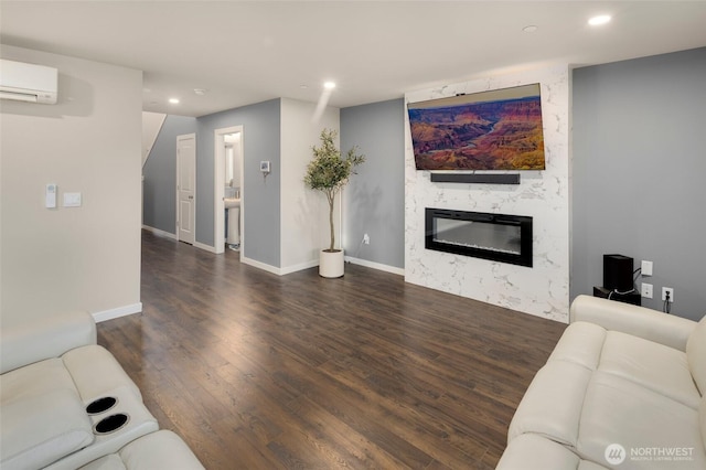 living area featuring a wall unit AC, wood finished floors, baseboards, recessed lighting, and a high end fireplace