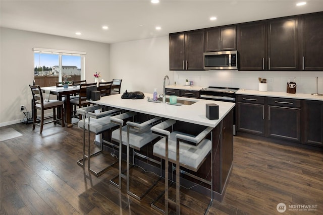 kitchen featuring a breakfast bar, recessed lighting, a sink, dark wood-type flooring, and appliances with stainless steel finishes