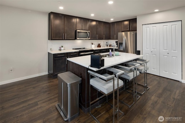 kitchen with a breakfast bar, dark wood-style flooring, a sink, stainless steel appliances, and dark brown cabinets