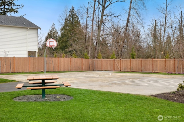 view of sport court with basketball hoop, a yard, and fence