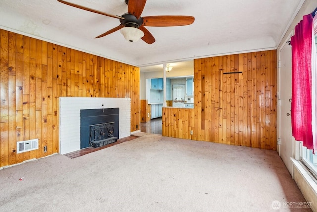 unfurnished living room featuring visible vents, carpet, wooden walls, and a ceiling fan