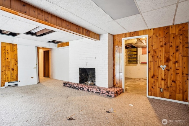 unfurnished living room featuring a baseboard heating unit, wood walls, carpet flooring, a fireplace, and a paneled ceiling