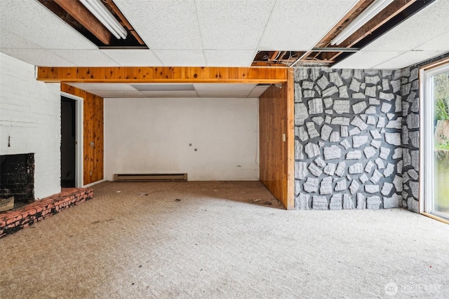 interior space with a drop ceiling, a baseboard heating unit, a brick fireplace, and carpet flooring