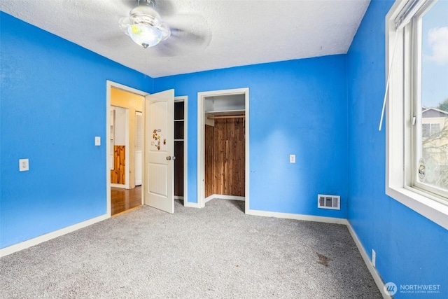 unfurnished bedroom with visible vents, carpet floors, a textured ceiling, and baseboards