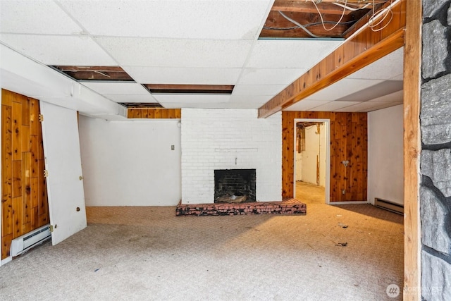 unfurnished living room featuring a drop ceiling, baseboard heating, wood walls, and a fireplace