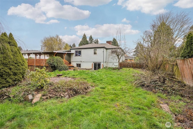 rear view of house with a chimney, a lawn, a wooden deck, and fence