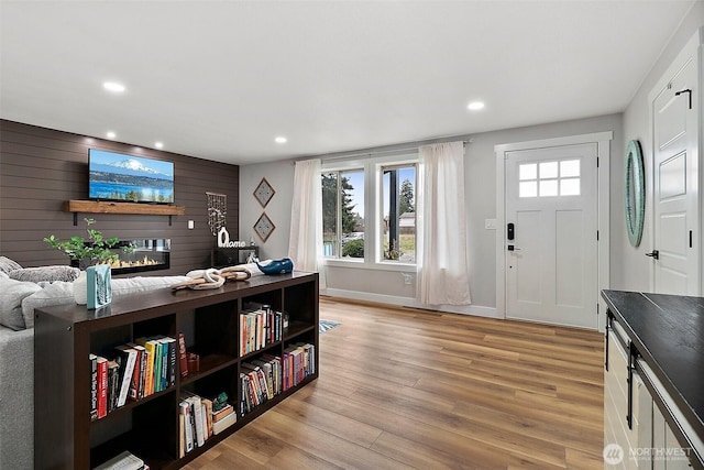 foyer with wooden walls, baseboards, recessed lighting, light wood-type flooring, and a large fireplace