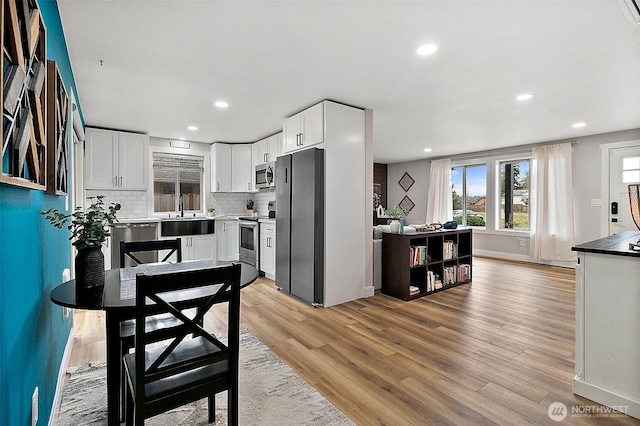 kitchen with a sink, white cabinets, light wood-style floors, appliances with stainless steel finishes, and tasteful backsplash