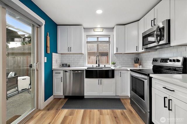 kitchen with light wood finished floors, a sink, light countertops, appliances with stainless steel finishes, and white cabinetry