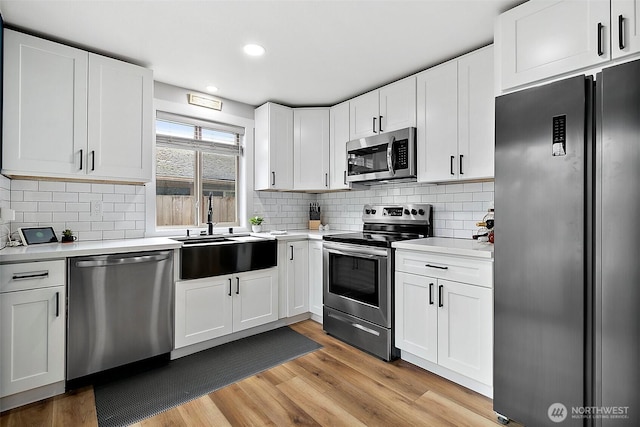 kitchen with a sink, stainless steel appliances, light wood-type flooring, and light countertops