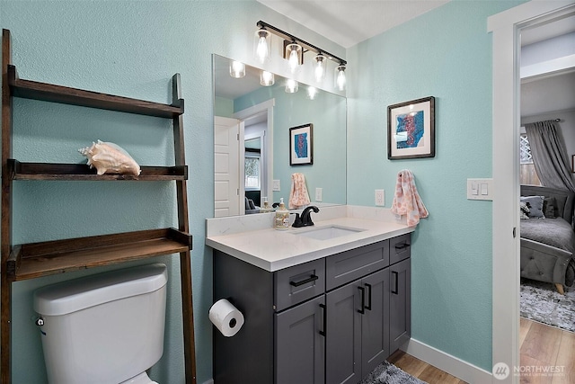 ensuite bathroom with baseboards, toilet, vanity, wood finished floors, and ensuite bath