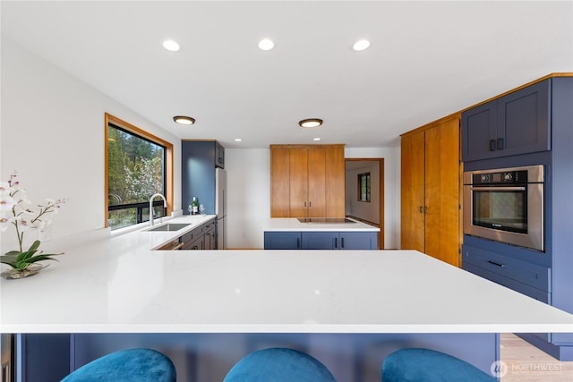 kitchen with oven, light countertops, a peninsula, freestanding refrigerator, and a sink