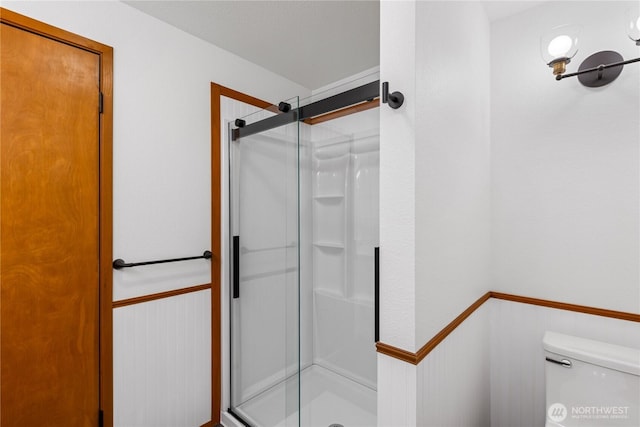 full bath featuring a wainscoted wall, toilet, and a stall shower