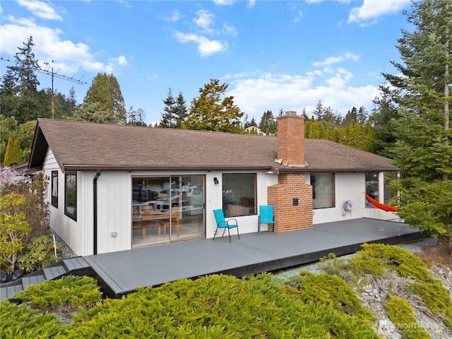 back of property with a chimney, a wooden deck, and roof with shingles