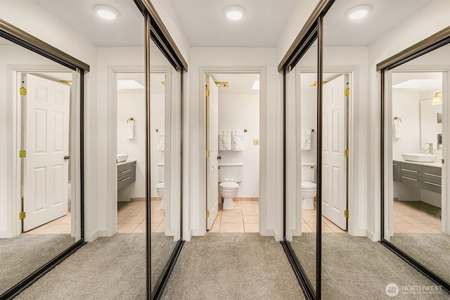 hallway with light tile patterned floors, light colored carpet, and a sink