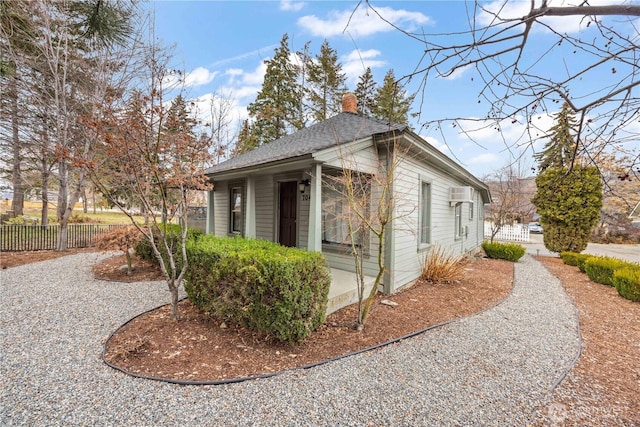 view of home's exterior with an AC wall unit, a shingled roof, a chimney, and fence