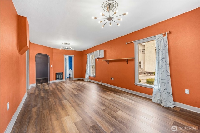 unfurnished living room with an inviting chandelier, heating unit, wood finished floors, and arched walkways